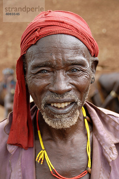 Portrait lächelnder Mann vom Volk der Hamar mit rotem Kopftuch und bunter Halskette auf dem Markt von Dimeka Äthiopien