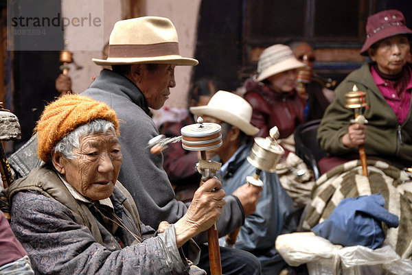 Alte tibetische Pilger sitzen im Hof mit Gebetsmühlen Lhasa Tibet China