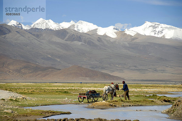 Mann mit Pferd und Kutsche am Fluß vor schneebedeckten Bergen bei Old Tingri Tibet China