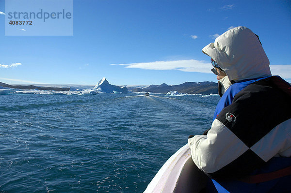 Warm angezogener Mensch blickt aus offenem Motorboot auf das Eismeer mit Eisbergen Sermilik Fjord Ostgrönland