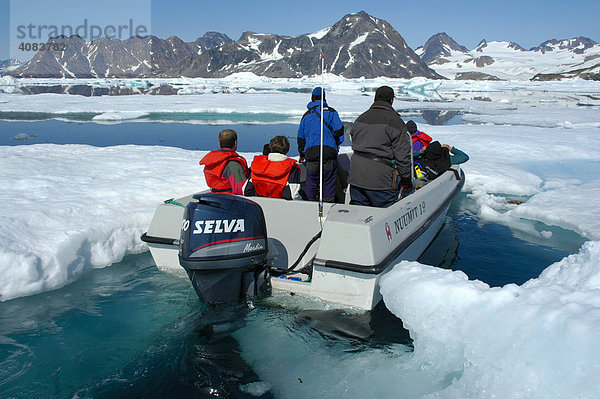 Offenes Motorboot mit warm angezogenen Menschen fährt durchs Packeis Ammassalik Fjord Ostgrönland