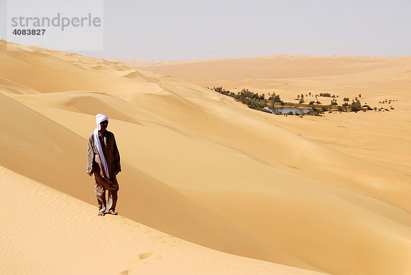 Tuareg geht durch Wüstensand und blickt auf Oase in der Ferne Um el Ma Mandara Libyen