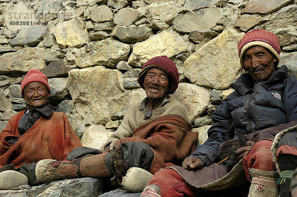 Drei freundliche Männer in traditioneller Wollkleidung sitzen vor einer Mauer Phu Nar-Phu Annapurna Region Nepal