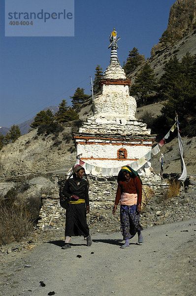 Zwei Frauen laufen vor einem weißen Stupa entlang Mungji Annapurna Region Nepal