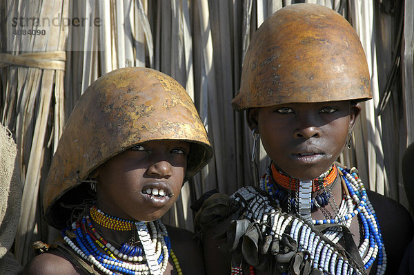 Zwei bunt geschmückte Mädchen vom Volk der Arbore mit Helm Kalebasse vor Strohhütte bei Weyto Äthiopien