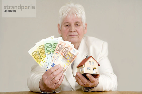 Alte Frau mit Hausmodell und Bargeld.