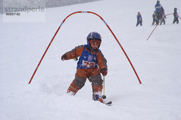 Kind beim Skifahren fährt durch Torbogen beim Abfahrtsrennen
