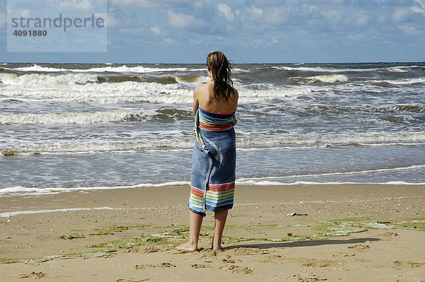 Junge Frau in ein Handtuch eingewickelt schaut auf das Meer  Katwijk aan Zee  Südholland  Holland  Niederlande