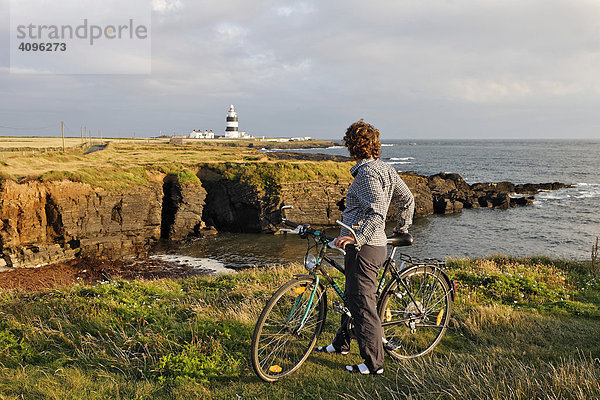 Radfahrerin blickt zum Leuchtturm am Hook¥s Head wo schon im 13. Jahrhundert ein Leuchtturm zu finden war  County Wexford  Irland