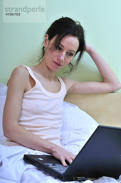 Portrait einer erwachsenen Frau  allein mit Laptop im Bett des Schlafzimmers