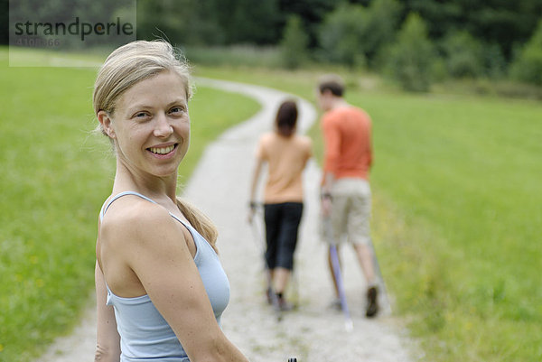 Junge Frau beim Nordic Walking hinter einem Pärchen