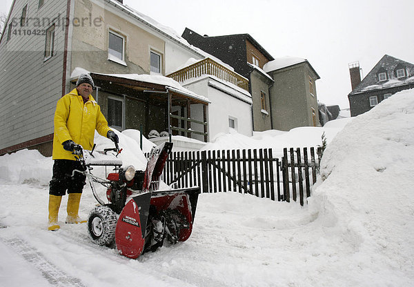 Mann räumt Schnee am Gartenzaun mit einer Schneefräsemaschine in Oberwiesenthal  Erzgebirge  Sachsen  Deutschland