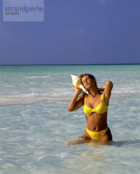 Junge Frau mit grosser Muschel am Ohr  Meeresrauschen  Meer  Malediven