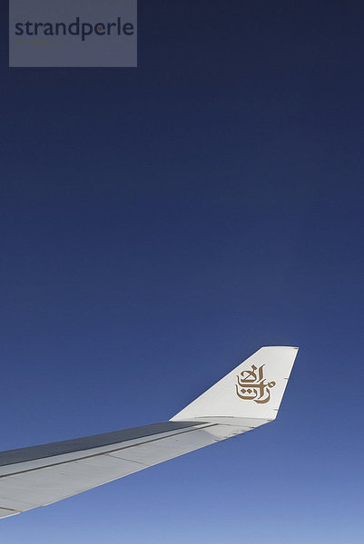 Tragfläche einer Airbus 330-200 der Fluggesellschaft Emirates vor blauem Himmel