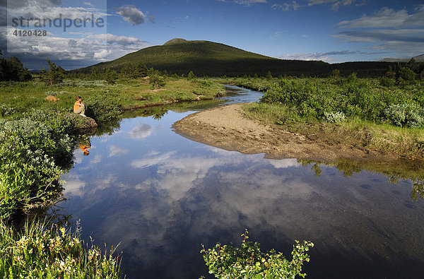 Eine Frau sitzt an einem Fluss im Jotunheimen Nationalpark  Norwegen