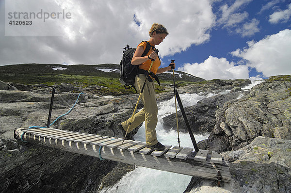 Trekking  Frau wandert über eine Holzbrücke  Jotunheimen Nationalpark  Norwegen