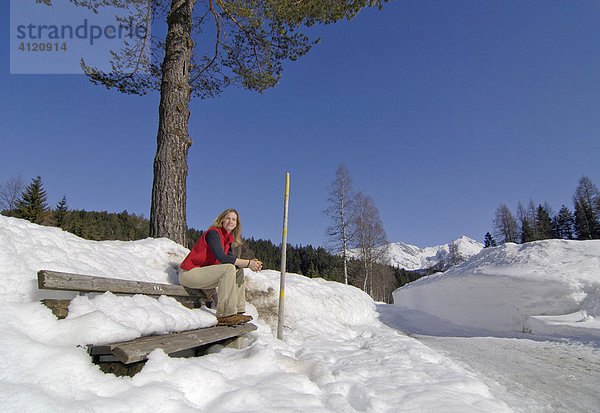 Eine Frau sitzt auf einer Holzbank in verschneiter Landschaft  Leutasch  Tirol  Österreich