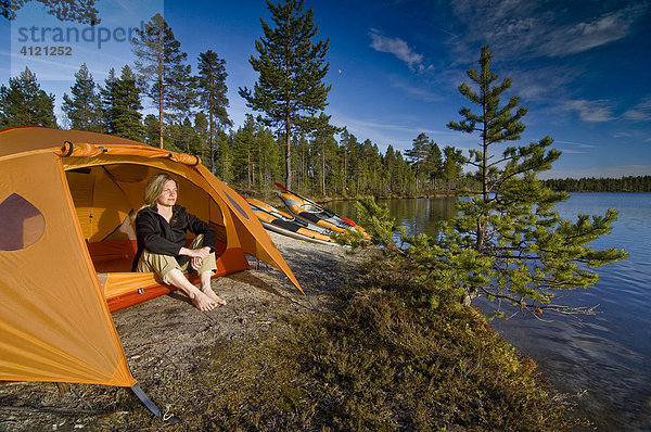 Frau sitzt vor einem Zelt am Seeufer  blickt in die Ferne Femundsmarka Nationalpark  Femundsmark  Norwegen