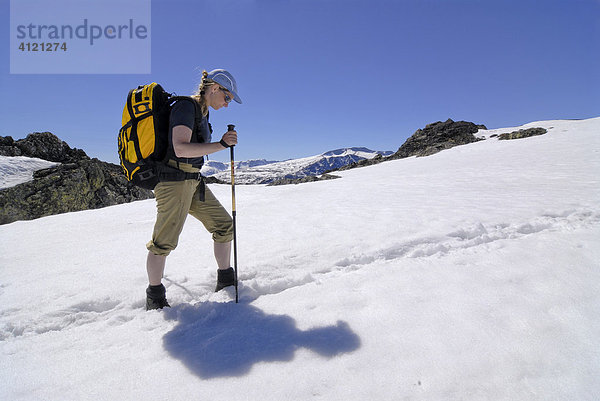 Frau mit Rucksack und Wanderstock stapft durch ein Schneefeld bei einer Bergtour  Jotunheimen Nationalpark  Vaga  Oppland  Norwegen