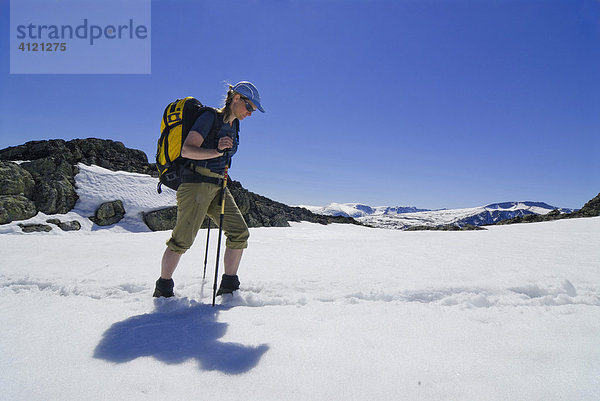 Frau mit Rucksack und Wanderstock stapft durch ein Schneefeld bei einer Bergtour  Jotunheimen Nationalpark  Vaga  Oppland  Norwegen