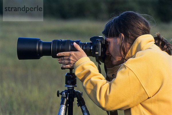 Fotografin mit gelber Jacke fotografiert mit einer Kamera am Stativ mit großem Objektiv