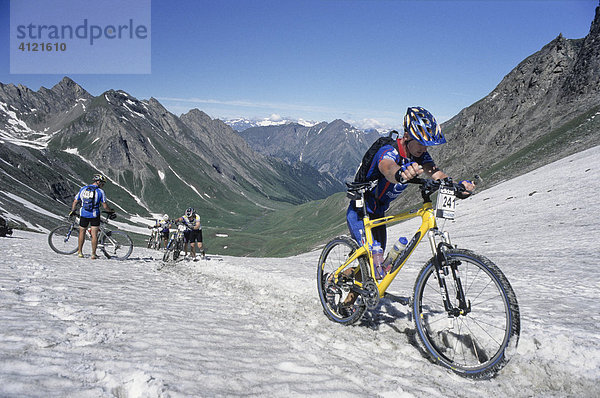 Teilnehmer der Adidas Bike Transalp Challenge  Mountainbikerennen  überqueren einen verschneiten Bergpass und schieben ihre Bikes durch den Schnee nach oben  Pfunderer Joch  Südtirol  Italien  Europa