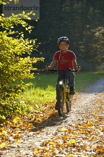 Kind fährt Rad auf einem Waldweg im Herbst