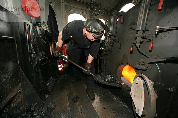 Lokomotivführer heizt den Kessel einer historischen Dampflokomotive ein