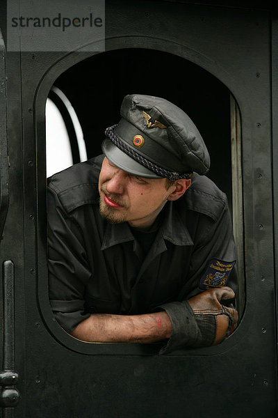 Lokführer schaut aus dem Fahrerhaus einer historischen Dampflokomotive