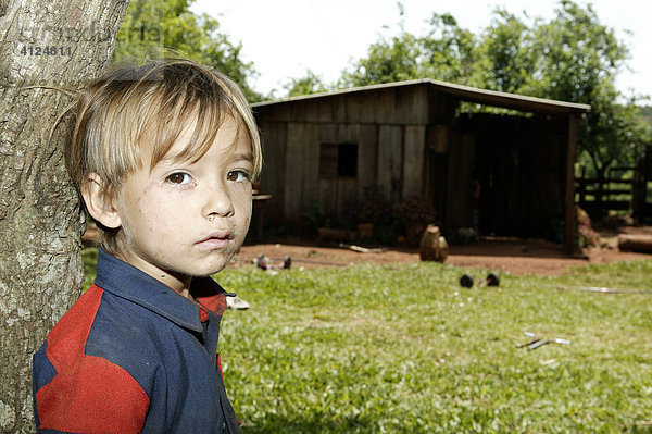 Junge lehnt an einem Baumstamm vor einem Haus  Paraguay  Südamerika