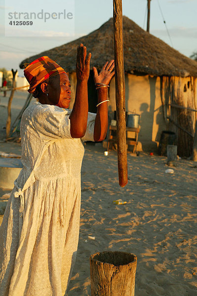 Alte Frau stampft Hirse vor einer Rundhütte  Sehitwa  Botswana  Afrika