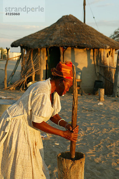 Alte Frau stampft Hirse vor einer Rundhütte  Sehitwa  Botswana  Afrika