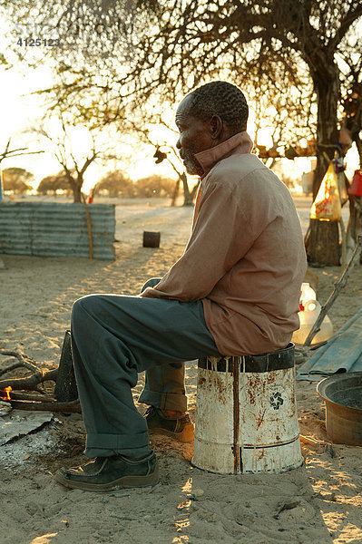 Mann genießt Morgensonne am Feuer  Cattlepost Bothatoga  Botswana  Afrika