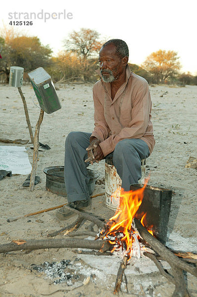 Mann genießt Morgensonne am Feuer  Cattlepost Bothatoga  Botswana  Afrika
