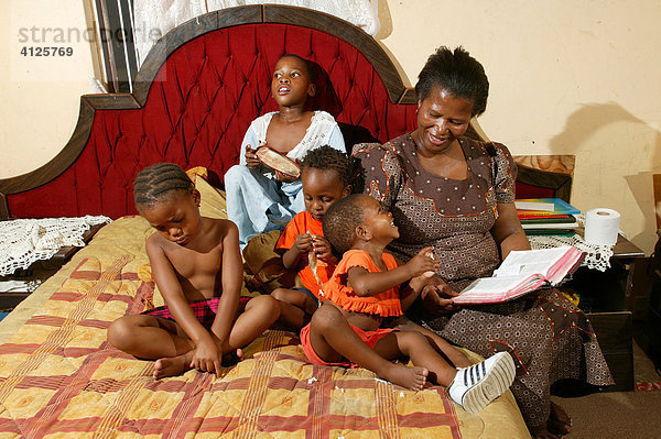 Mutter mit Kindern auf dem Bett liest vor  Gaborone  Botswana  Afrika