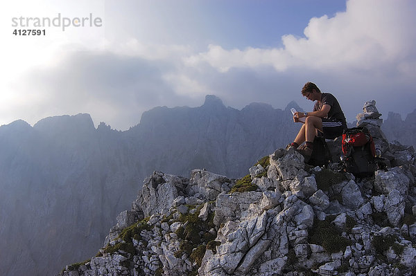 Bergsteiger sitzt auf dem Gipfel des Mitterkaiser  im Hintergrund der Wilde Kaiser  Tirol  Österreich