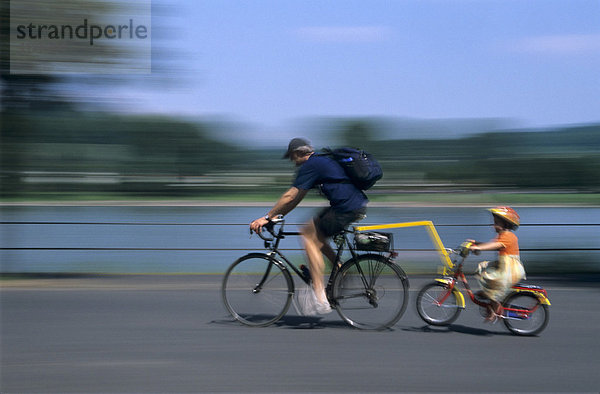 Radfahrer mit behelmtem Mädchen auf Trailer-Bike unterwegs