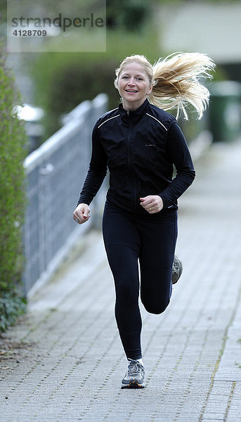 Junge  blonde Frau im schwarzen Sportanzug beim Jogging