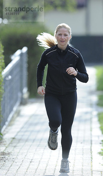 Junge  blonde Frau im schwarzen Sportanzug beim Jogging