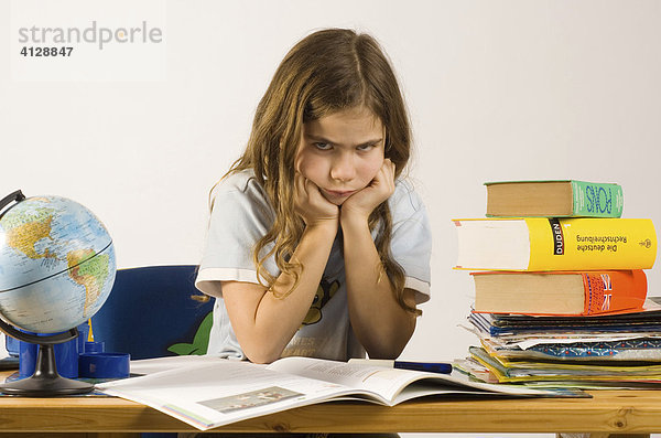 Mädchen  9 Jahre  sitzt böse blickend am Schreibtisch vor ihren Hausaufgaben