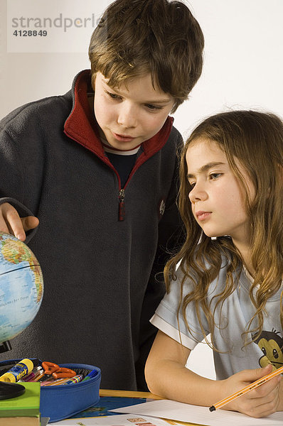 Geschwister  Junge (10 Jahre) und Mädchen (9 Jahre) bei Hausaufgaben an einem Globus