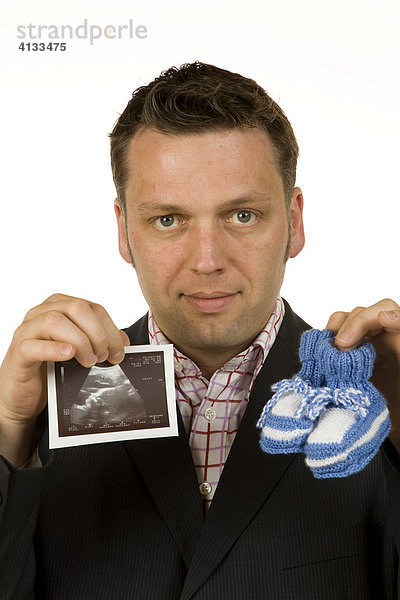 Geschäftsmann / Manager  40-jährig  hält Babyschuhe und Ultraschallbild