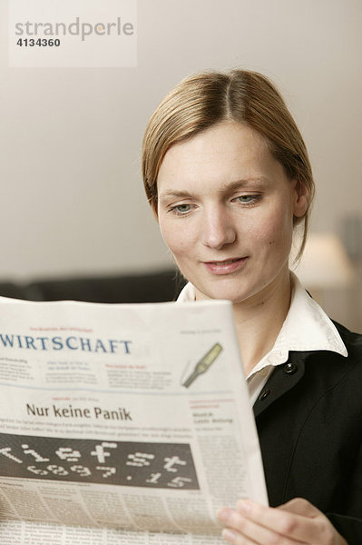 Junge blonde Frau mit Wirtschaftsteil einer Zeitung  lächelt