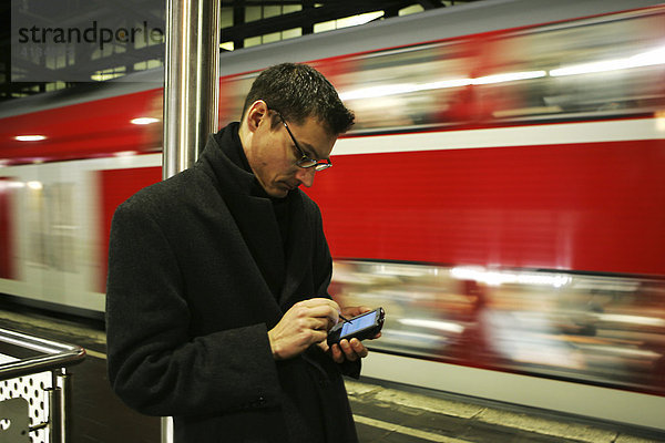 DEU Bundesrepublik Deutschland : Mann arbeitet mit seinem Pocket Computer PDA beim warten auf den Zug auf dem Bahnsteig.