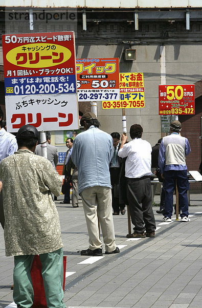 JPN  Japan  Tokio: Personen mit Werbeschildern stehen vor einem Ausgang des Bahnhofs von Shimbashi