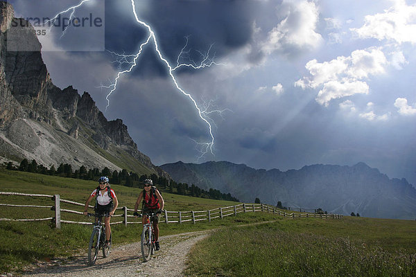 Mountainbike-Fahrerinnen im Gewitter mit Blitz am Peitlerkofel  Dolomiten  Italien