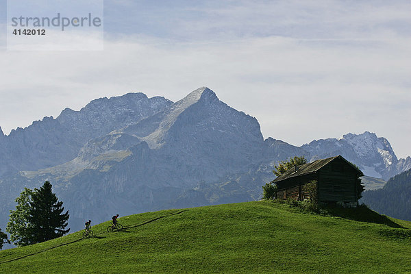 Zwei Mountainbiker an einer Hütte  hinten mit Hochblassen  Alpspitze und Zugspitze (von links nach rechts)  Oberbayern  Bayern  Deutschland