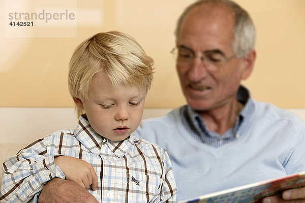 älterer Herr liest seinem Enkel aus einem Buch vor