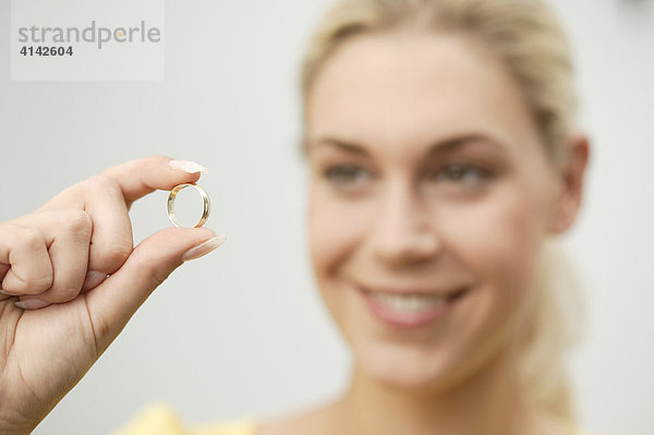 Junge  blonde Frau begutachtet lächelnd Ehering  Schärfe auf Ring