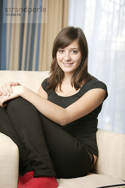 17-jähriges Mädchen mit roten Socken sitzt auf Sofa und lächelt